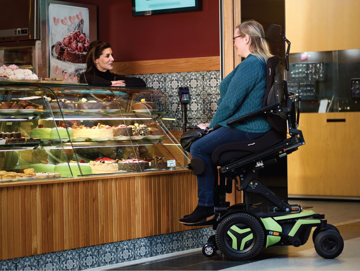 A lady in a Permobil F3 in ActiveReach at a counter in a store.